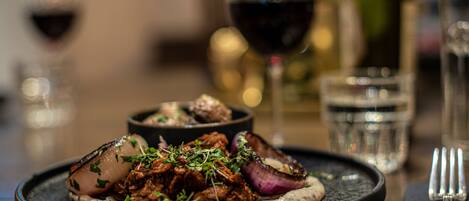 Un plato de comida con una copa de vino tinto y una botella al fondo.