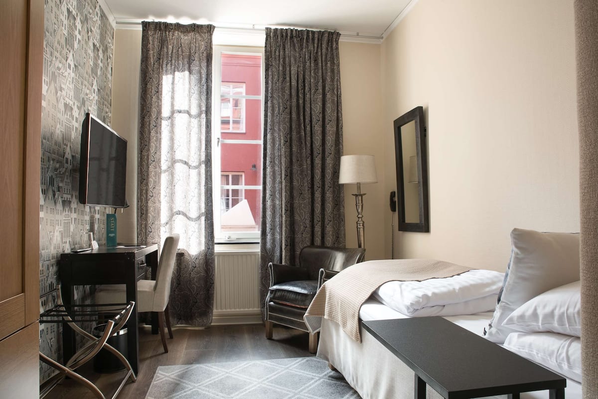 Une chambre d’hôtel comprenant un lit, un bureau avec une chaise, une télévision et une fenêtre avec des rideaux.