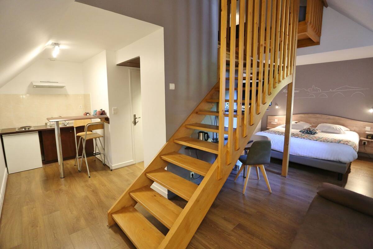 Een modern interieur met een houten trap, een keukenhoek en een slaapkamer met een bed en nachtkastje.