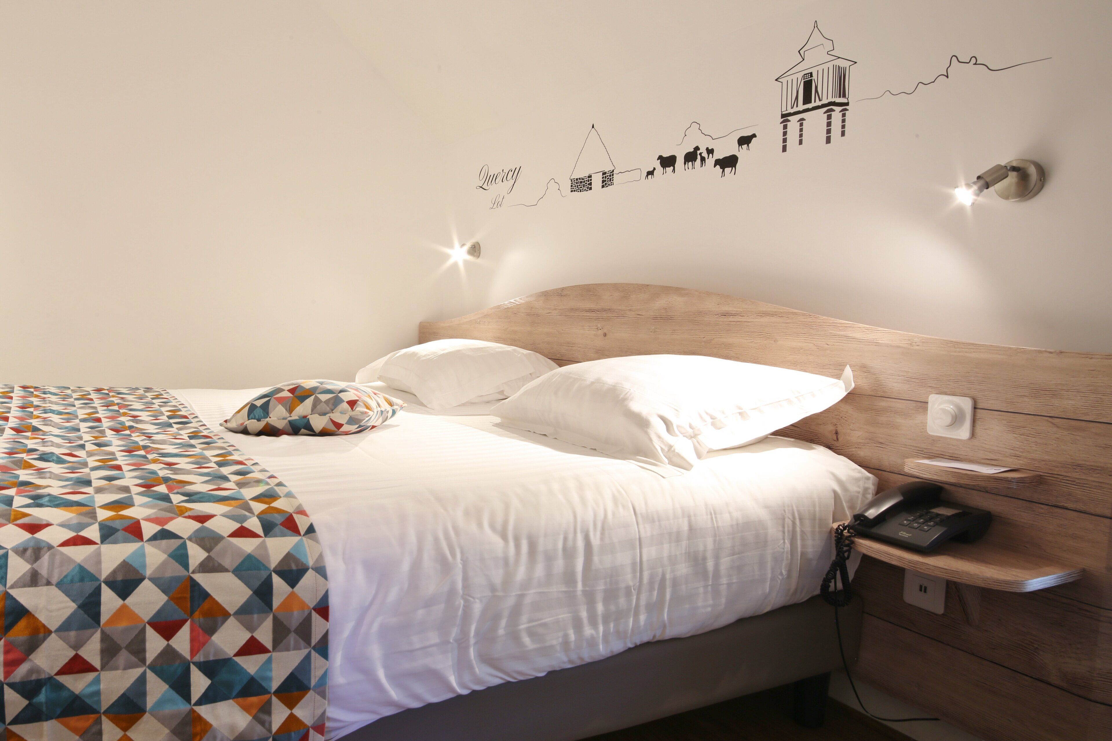 A neatly made bed with a patterned blanket, a bedside phone, and a wall decal with a line drawing of a building and animals.