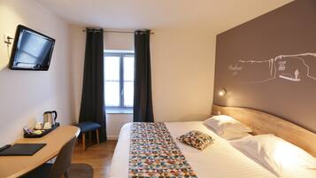 A hotel room with a bed, a desk, a chair, a television, and a window with curtains.