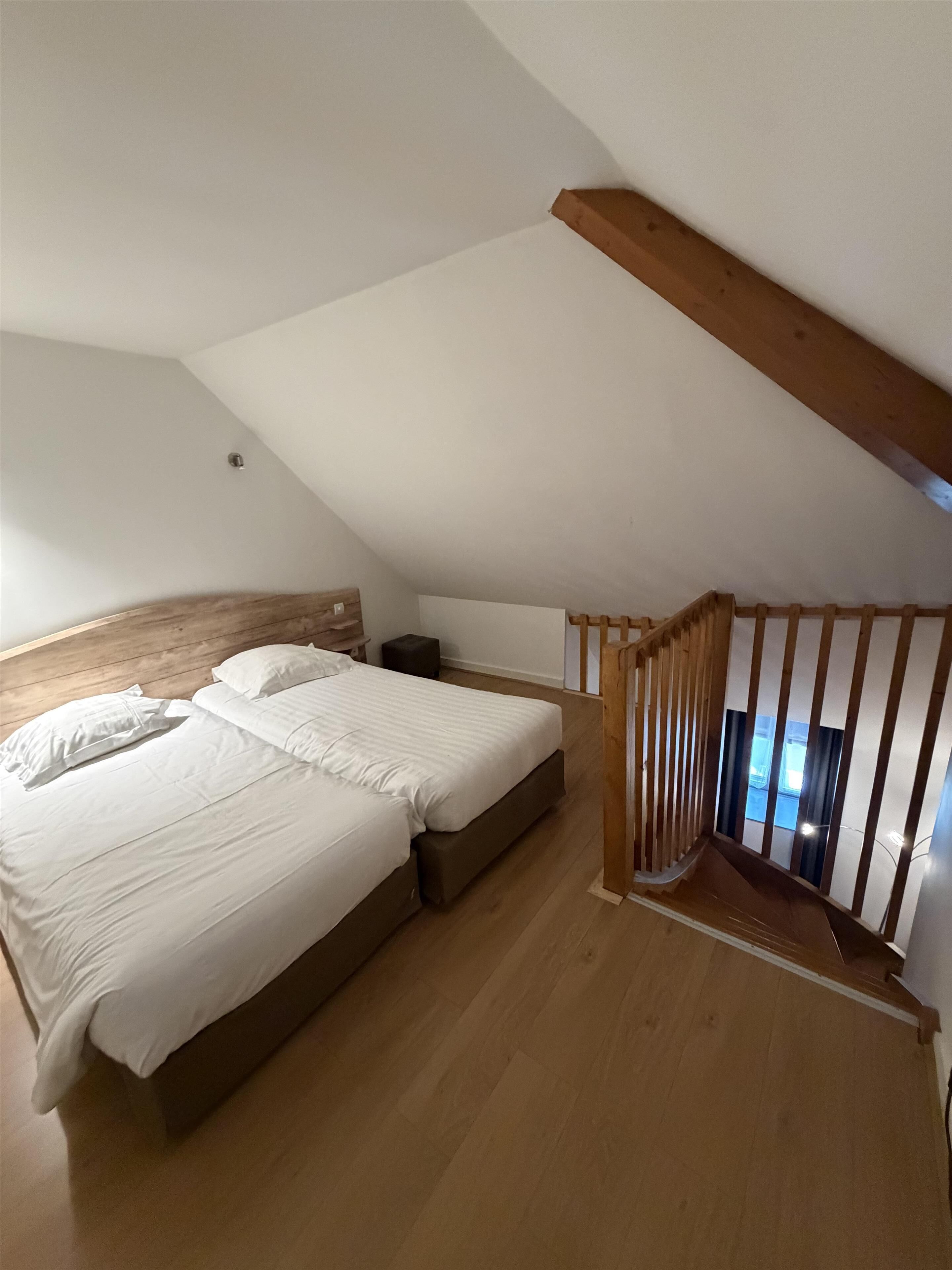 Un dormitorio con una cama de madera, una mesita de noche y un techo inclinado.