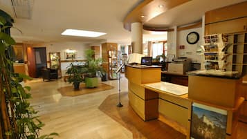 Un hall d’entrée spacieux avec un comptoir d’accueil, une grande horloge et diverses plantes.