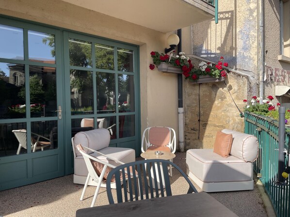 A sunlit patio with a green-framed window, white cushioned seating, and a small table.