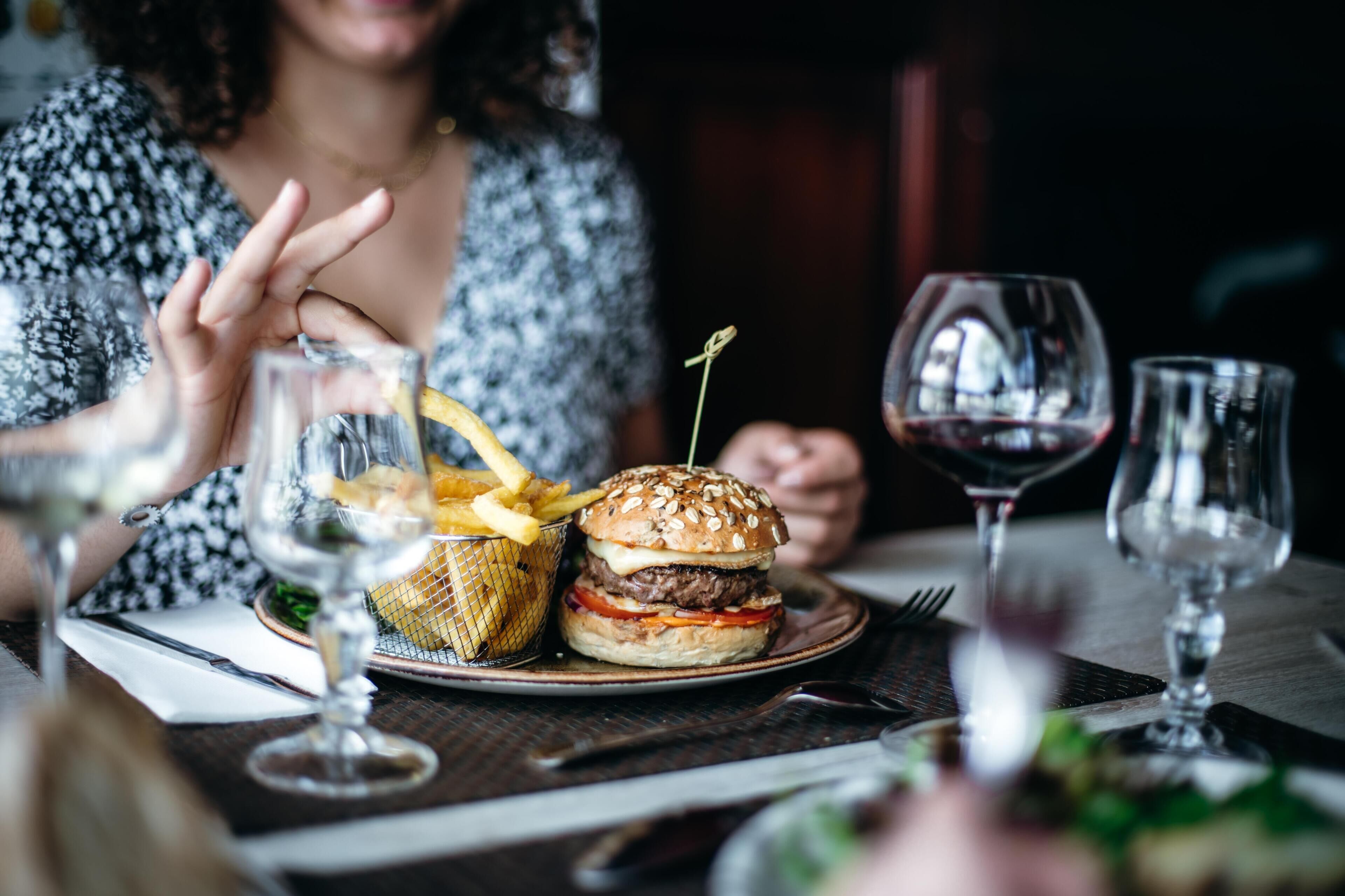 Ein Esstisch mit einem Burger, Pommes und Weingläsern.