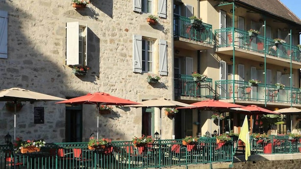 Un edificio de piedra con balcones, mesas al aire libre con sombrillas y macetas con flores.