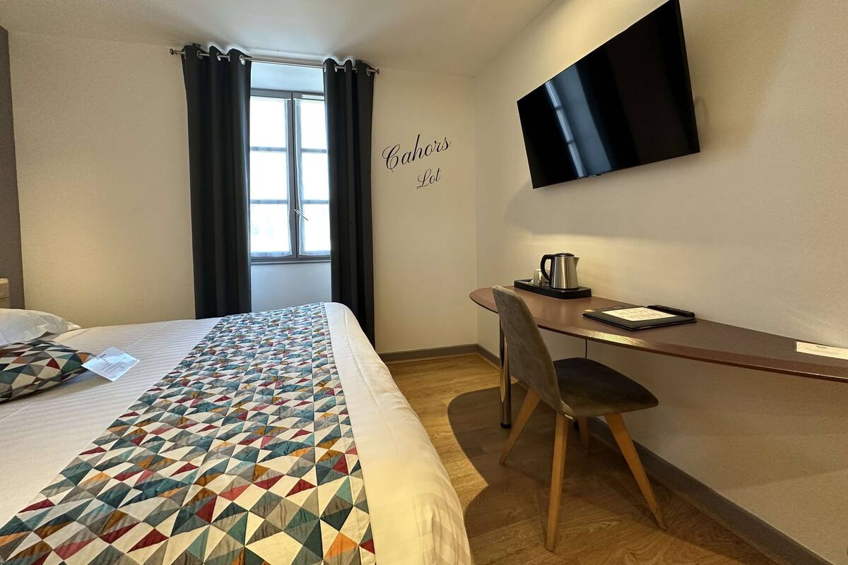 Een hotelkamer met een bed, een bureau, een stoel, een televisie en een raam met gordijnen.