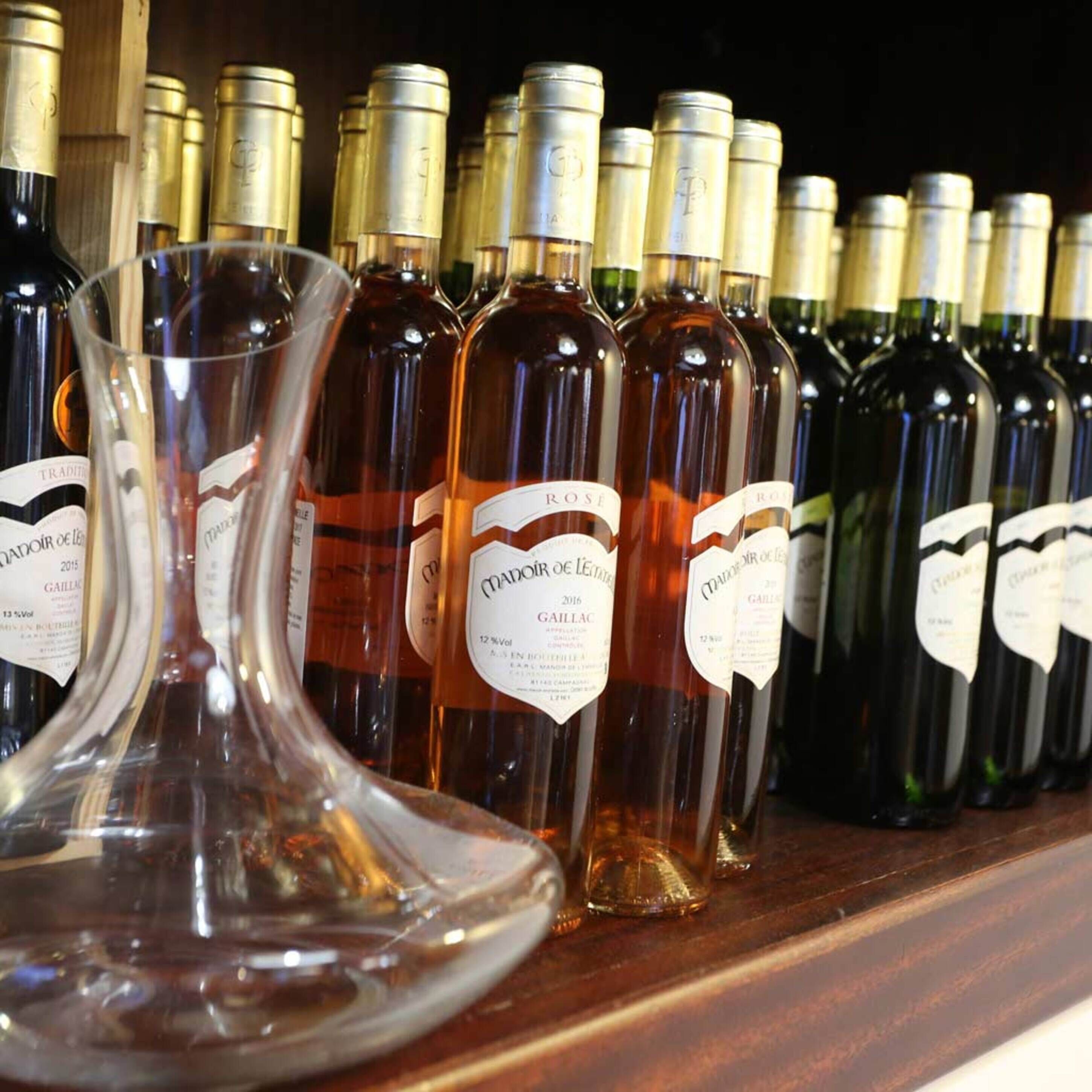 A row of wine bottles with labels, a clear wine glass, and a wooden shelf.