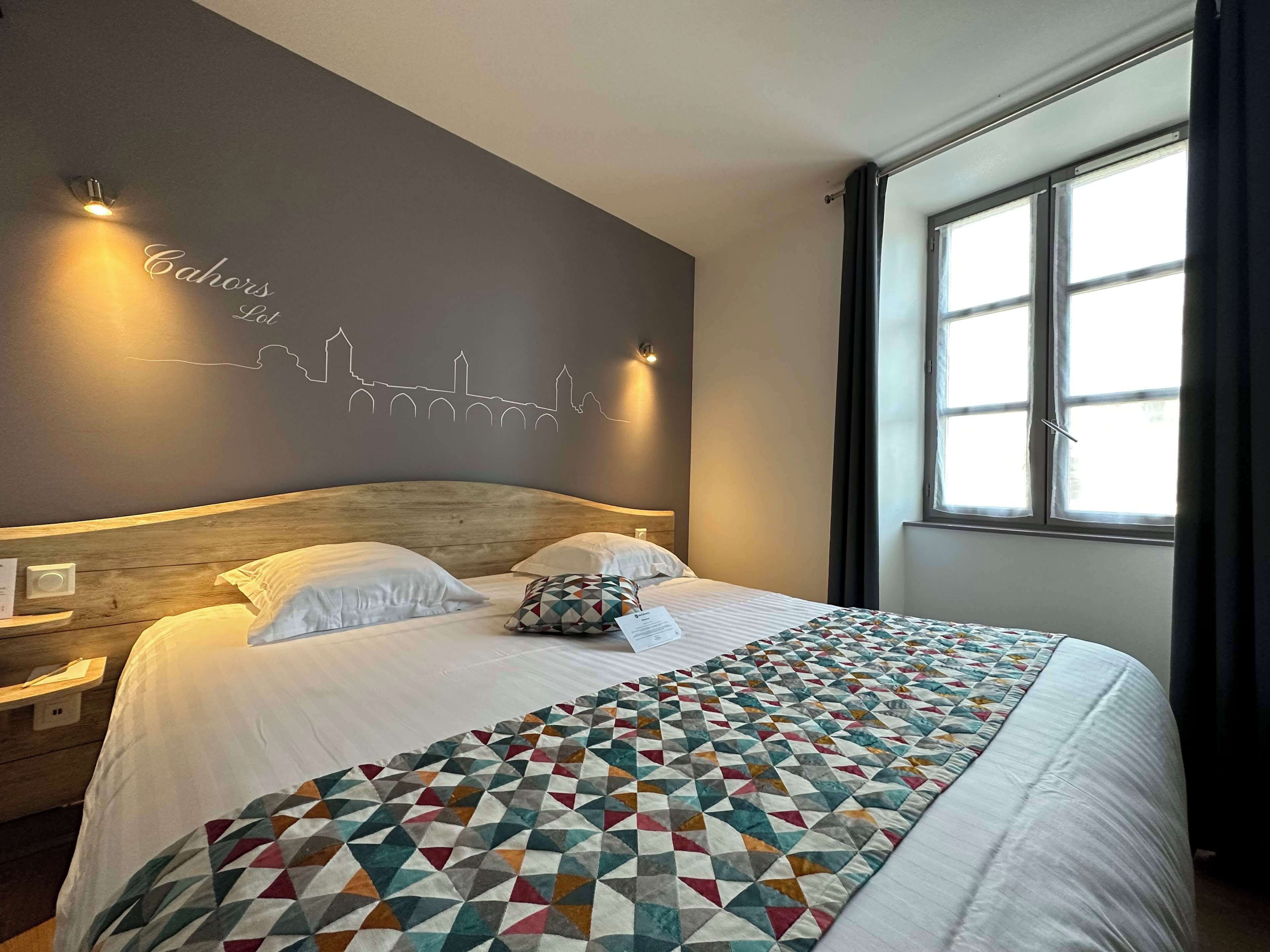 Una habitación de hotel con una cama, un cuadro de un horizonte urbano, una ventana con cortinas y una mesita de noche.