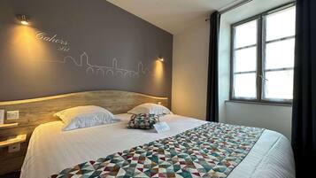 Una habitación de hotel con una cama, un cuadro de un horizonte urbano, una ventana con cortinas y una mesita de noche.