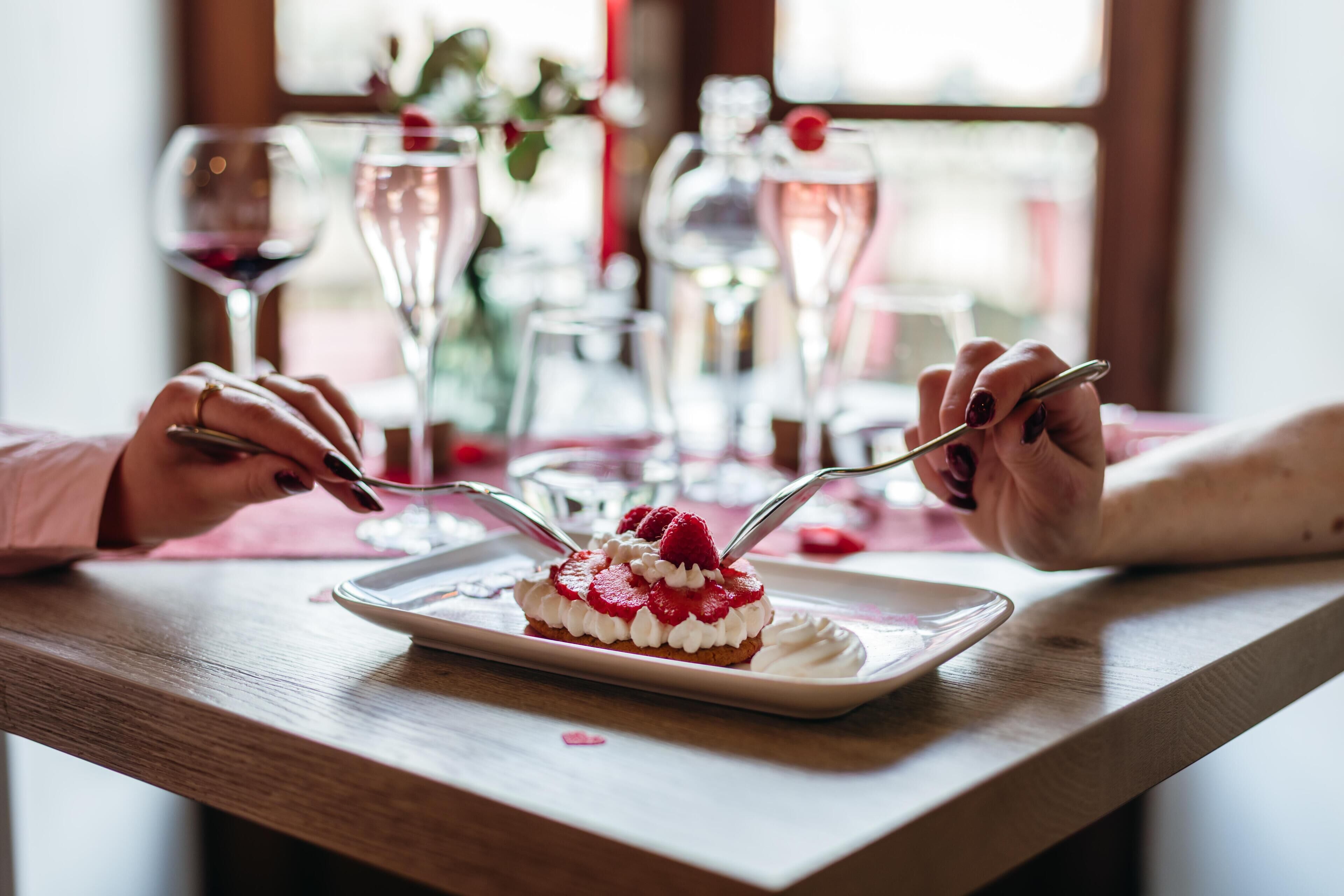 Un dessert servi sur une assiette blanche, accompagné d’une fourchette, est posé sur une table en bois recouverte d’une nappe rose.