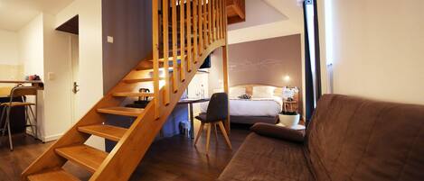 A modern interior with a wooden staircase, a bed, a sofa, and a dining area.