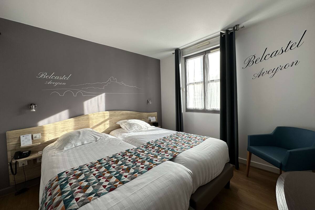 Een hotelkamer met een groot bed, een houten hoofdeinde, een bureau met telefoon en een stoel.