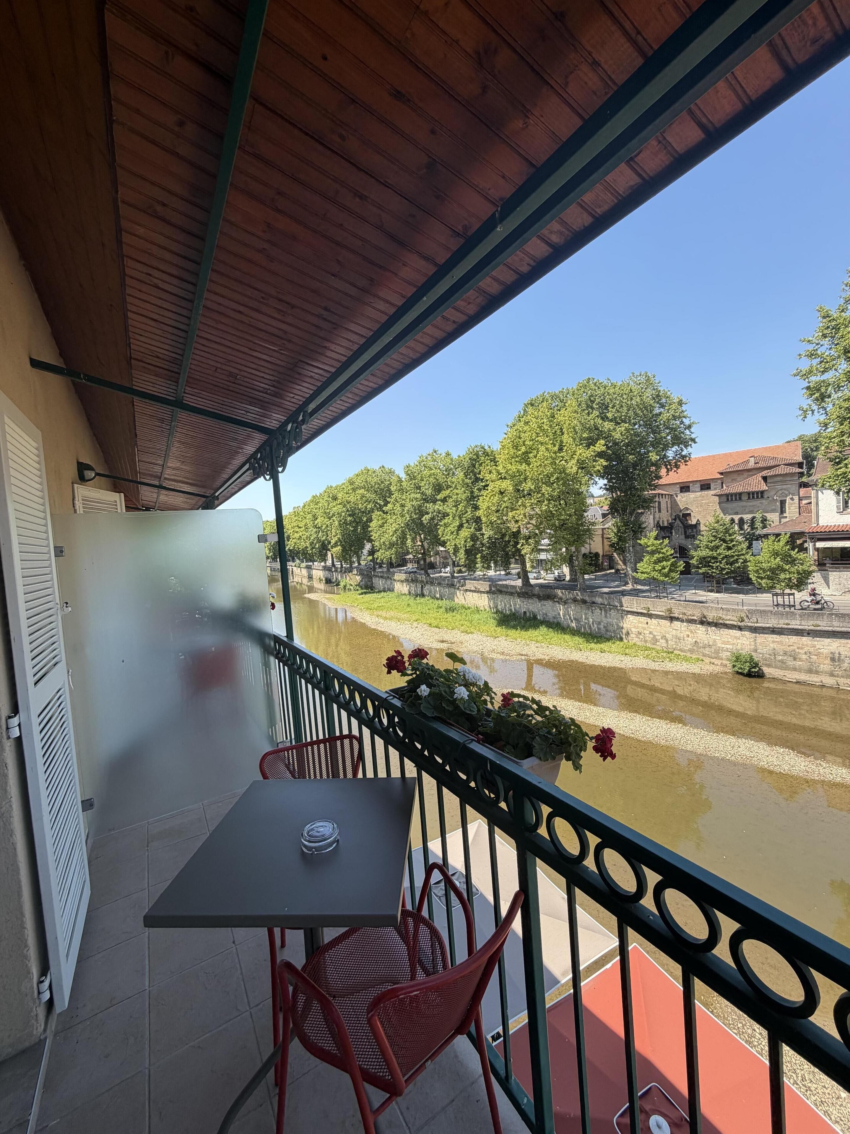 Un balcón con mesa y sillas, con vistas a un río y edificios.