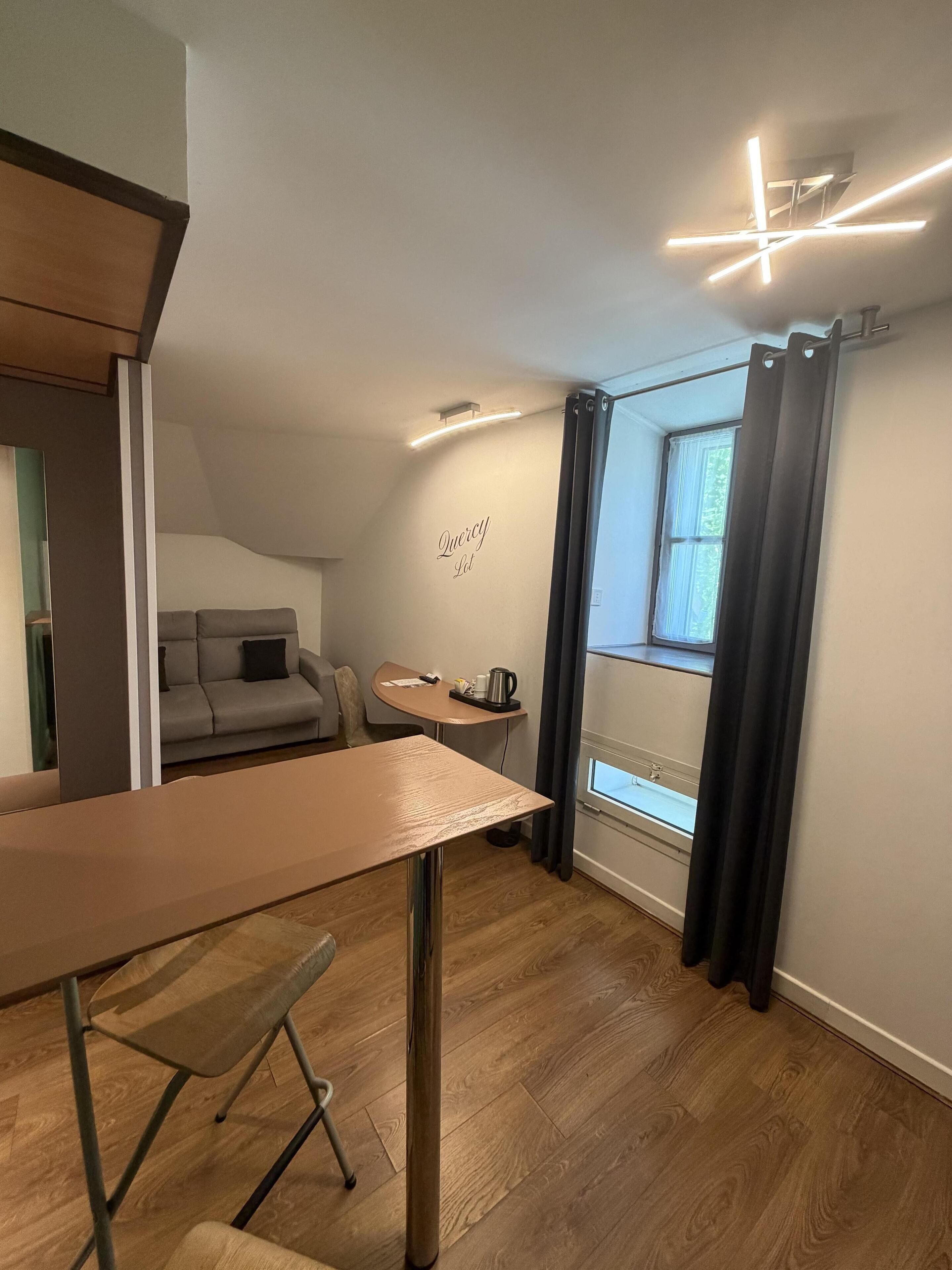 A modern interior with a dining table, a sofa, a small round table with a kettle, and a window with curtains.