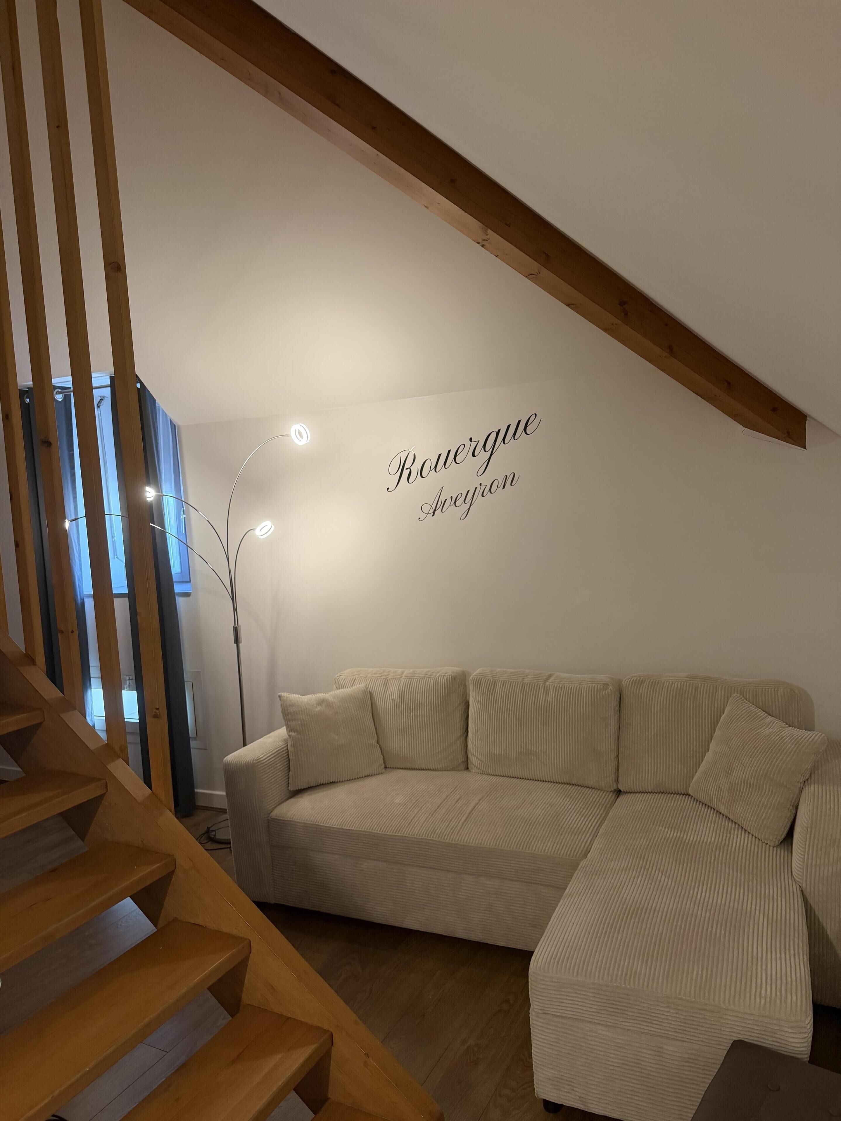 A modern living room with a sectional sofa, wooden staircase, and a wall-mounted light fixture.