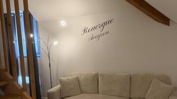A modern living room with a sectional sofa, wooden staircase, and a wall-mounted light fixture.