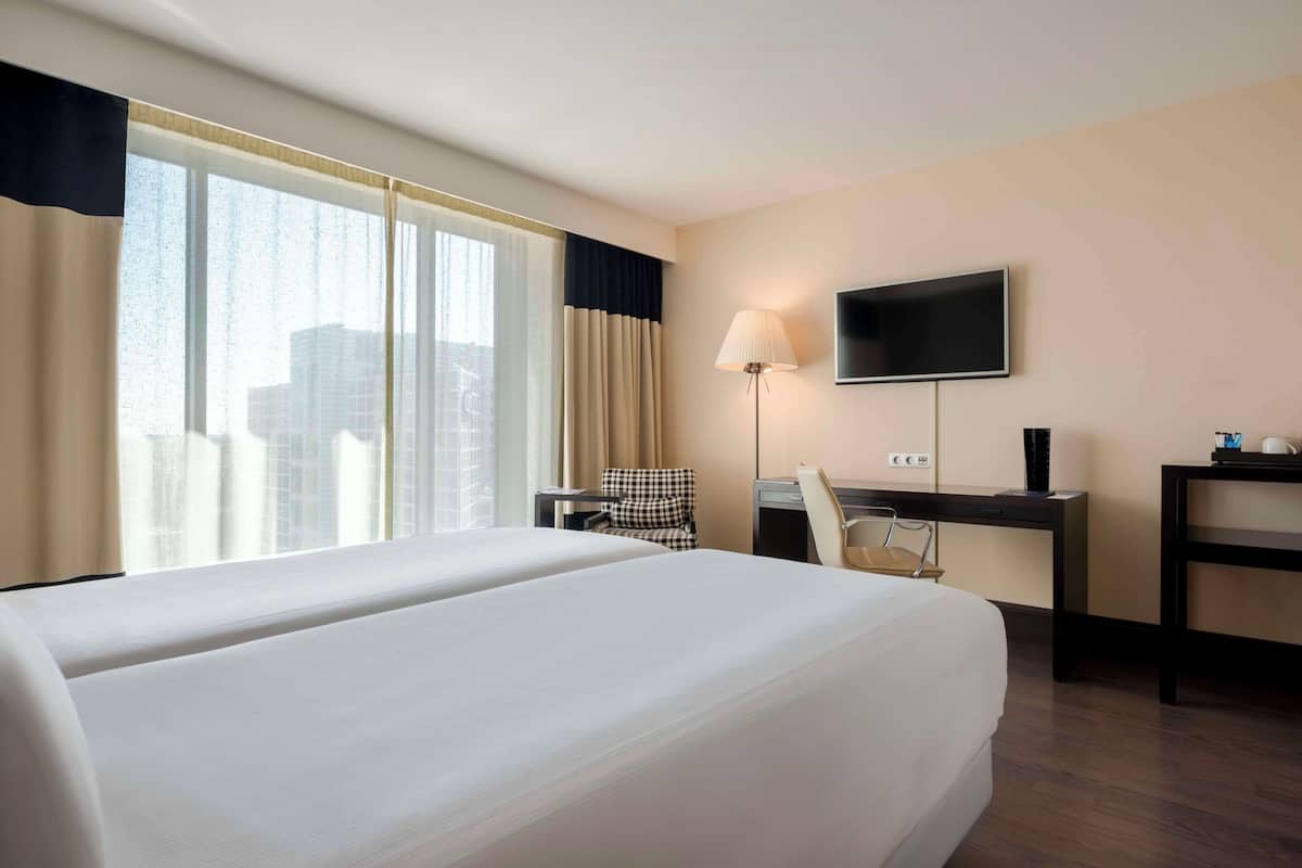 A hotel room with a large bed, a desk, a chair, a TV, and a window with curtains.