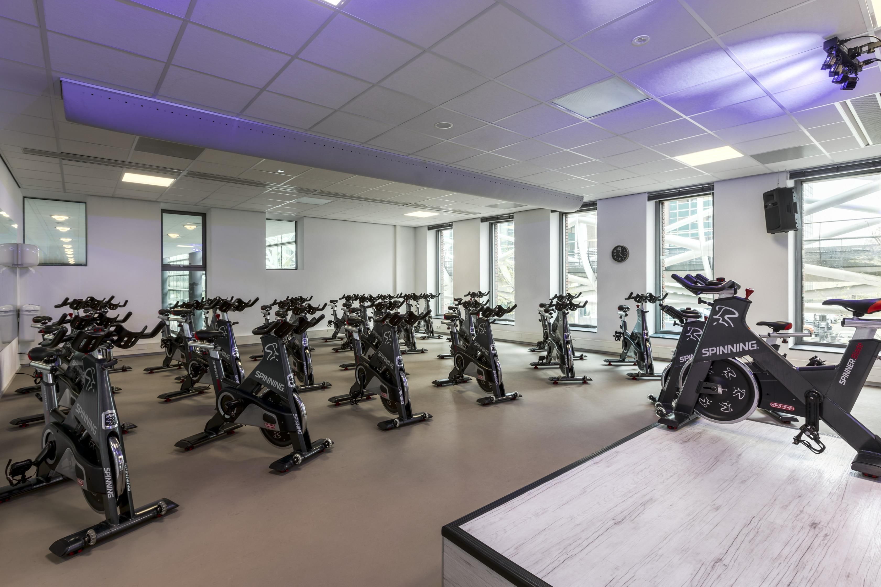 A gym with multiple stationary bikes, large windows, and a modern ceiling design.