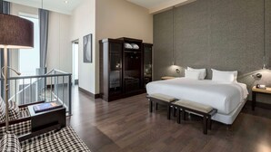 Une chambre d’hôtel moderne avec un grand lit, une banquette, une armoire et un bureau avec une lampe.