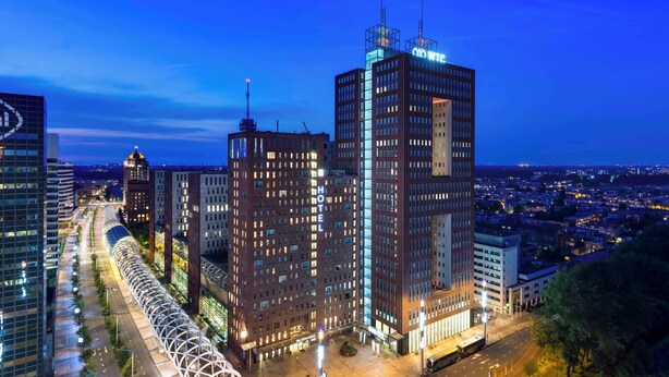 A modern hotel with a prominent glass facade, a rooftop pool, and a well-lit urban street view. - NH Den Haag (The Hague)