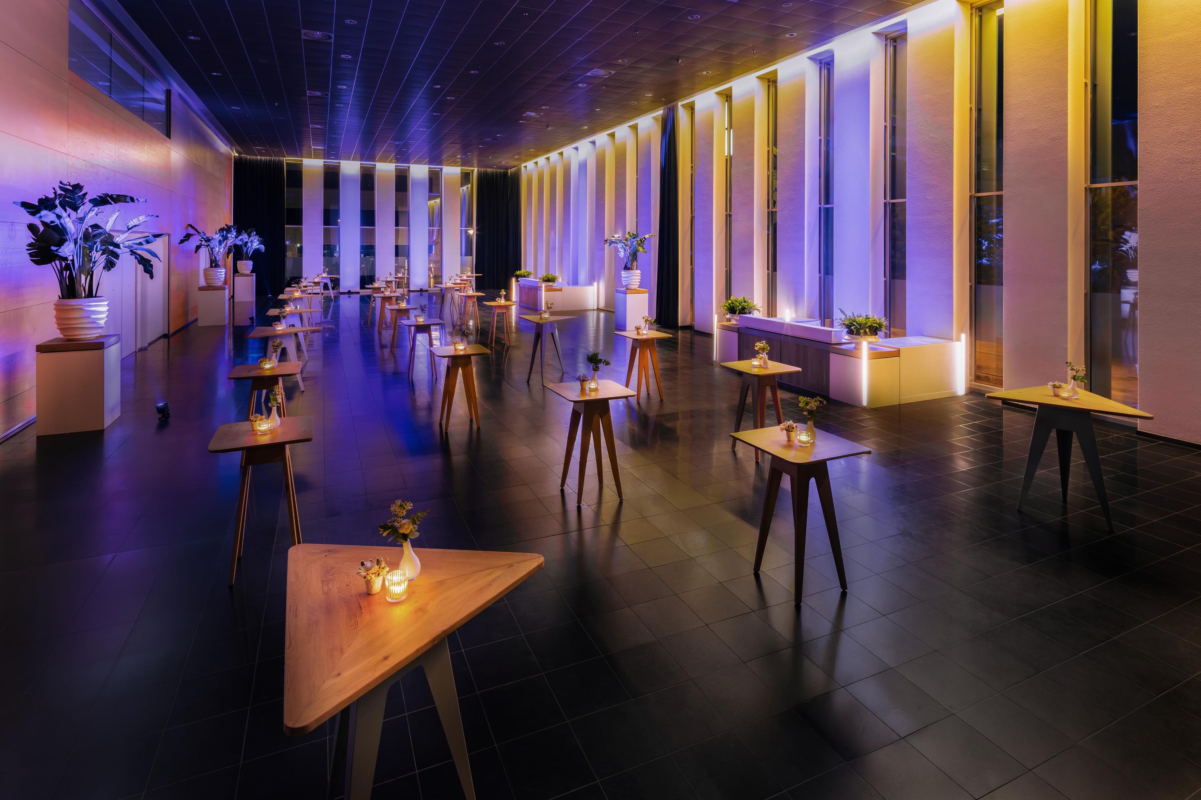 Un espace intérieur spacieux, doté de nombreuses tables et chaises, de grandes fenêtres et de plantes en pot.