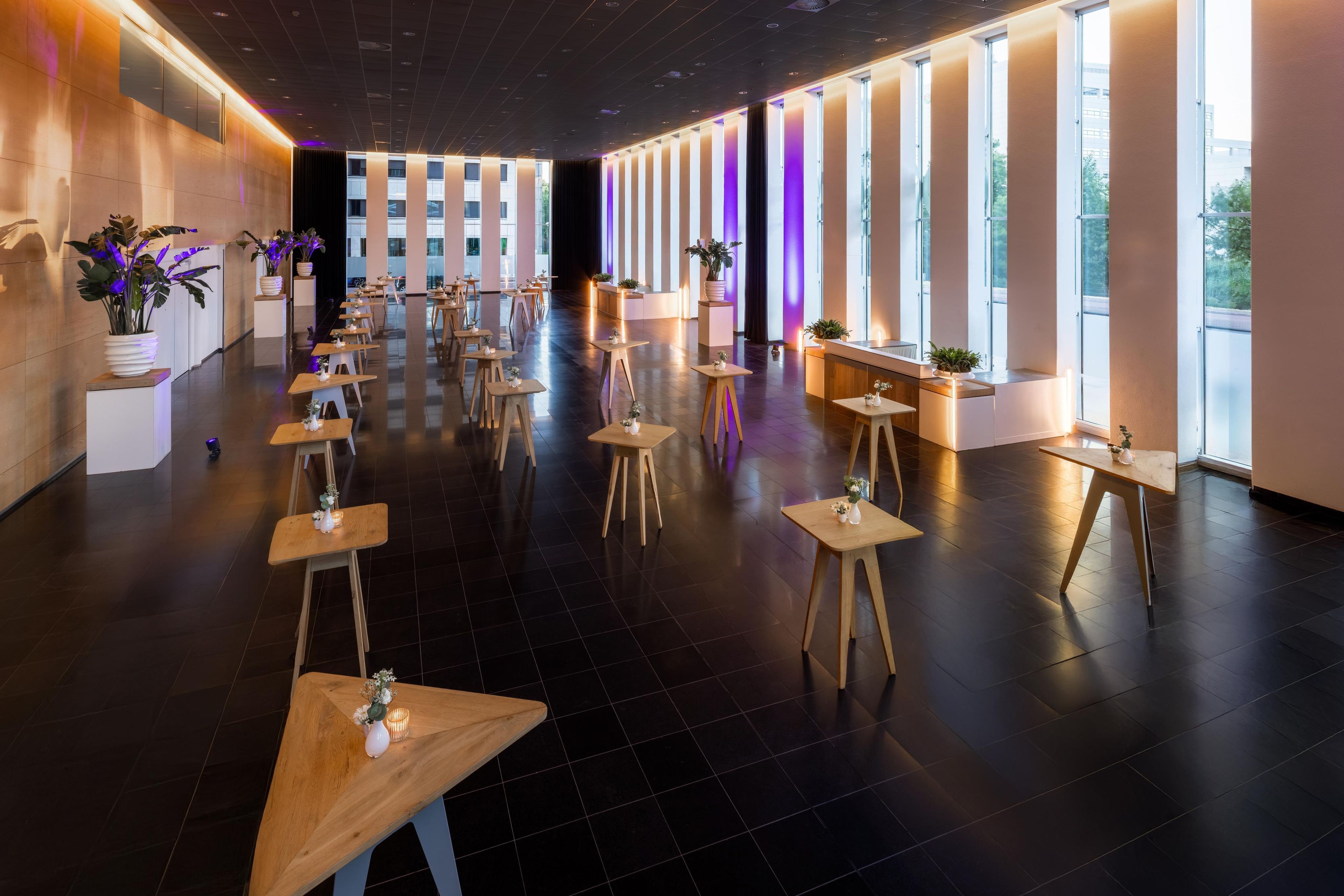 Een moderne hotel lobby met een lange receptiebalie, verschillende zithoeken en grote ramen.