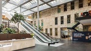 A spacious atrium with a glass ceiling, a central escalator, and a reception desk labeled "THINK TRADE CENTER." - NH Den Haag (The Hague)
