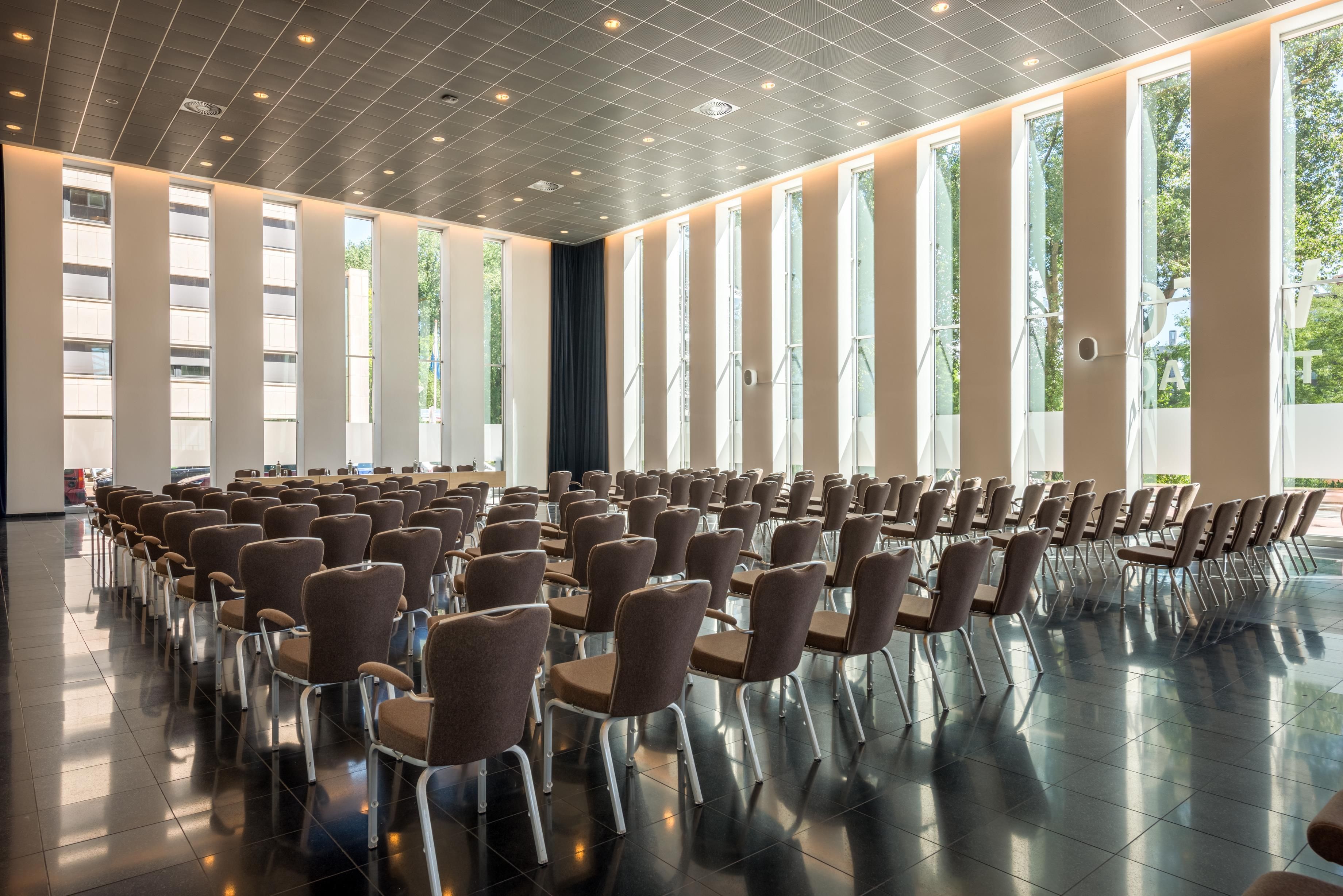 A conference room with rows of chairs, large windows, and a tiled floor.