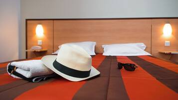 Una cama bien hecha con un edredón a rayas, una toalla doblada, un sombrero y un par de gafas de sol sobre la cama.