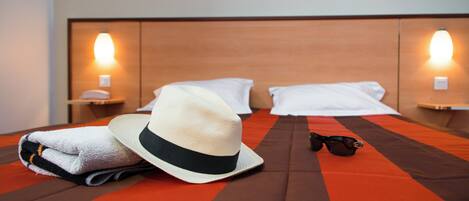 A neatly made bed with a striped bedspread, a folded towel, a hat, and a pair of sunglasses on the bed.