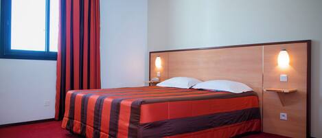 Ein Hotelzimmer mit Bett, rotem Teppich, Vorhängen, einem Fenster und Wandleuchten.