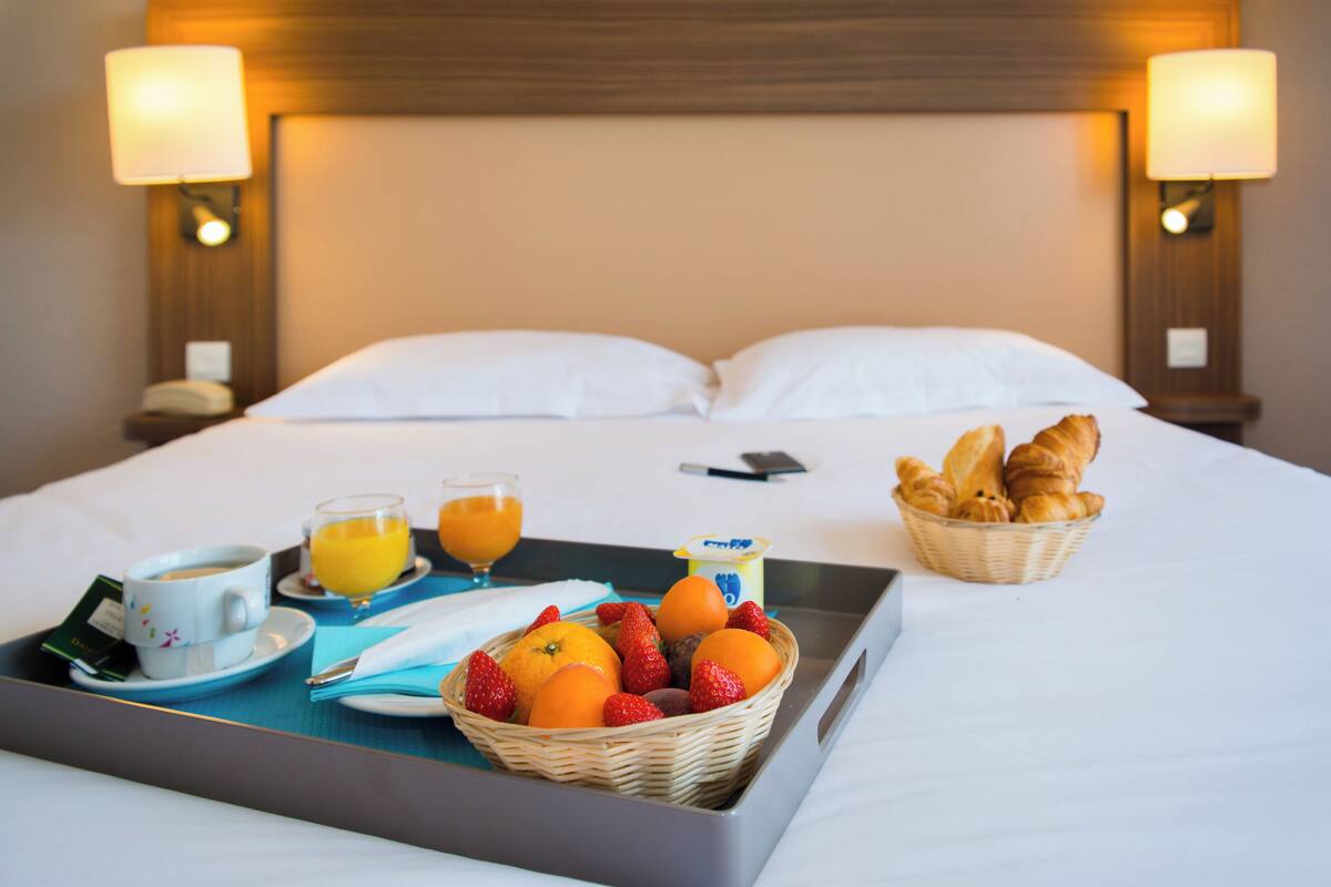 A neatly made bed with pillows, a tray with breakfast items, and a basket of croissants.