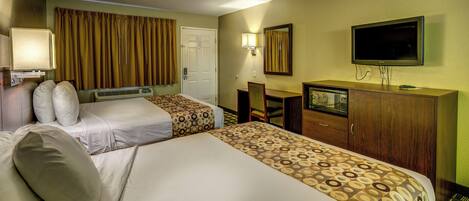 A hotel room with two beds, a desk, a television, and a mirror.