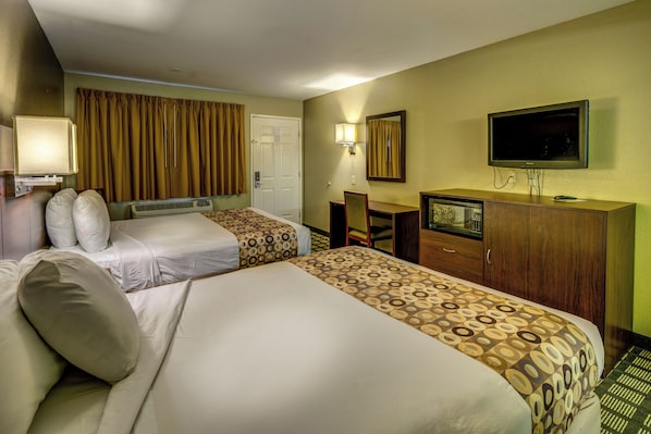 A hotel room with two beds, a desk, a television, and a mirror.