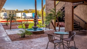 An outdoor patio with a fountain, seating, and a vending area. - Travelers Inn (Phoenix)