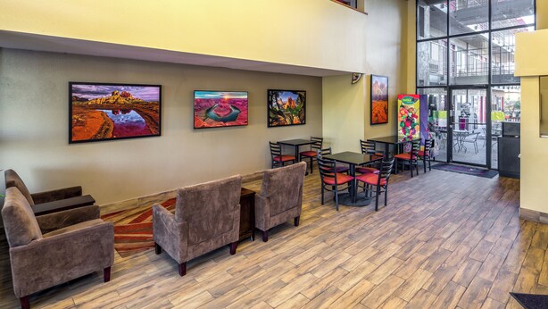 A lobby with a wooden floor, seating area with chairs and tables, and artwork on the walls. - Travelers Inn (Phoenix)