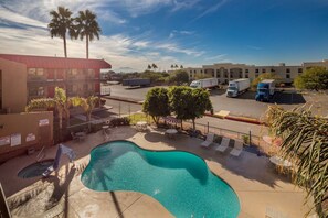 A swimming pool with lounge chairs, a red building, and a parking lot with trucks.