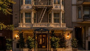 A multi-story building with a prominent fire escape, a corner entrance with a sign reading 'BUSH STREET,' and a well-lit facade. - Cornell Hotel (San Francisco)