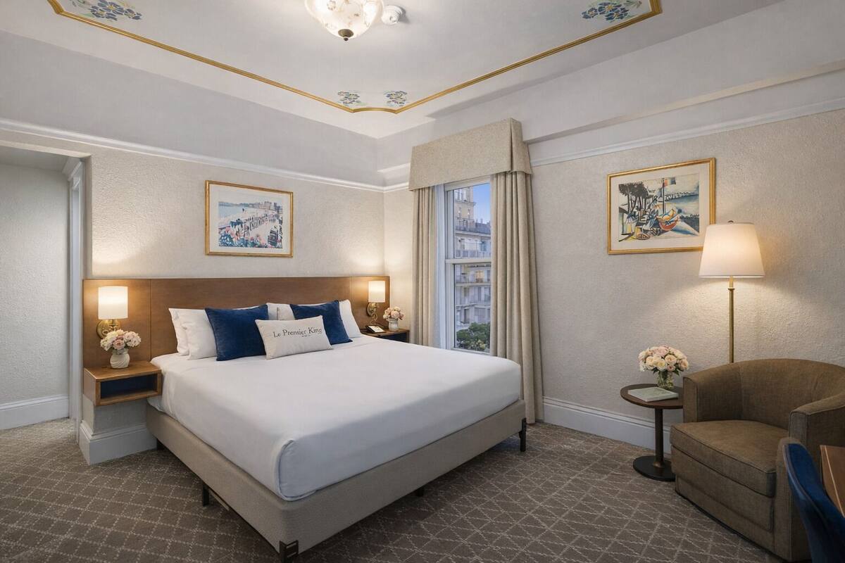 Une chambre d’hôtel avec un grand lit, une chaise, une table de chevet avec une lampe et une fenêtre avec des rideaux.