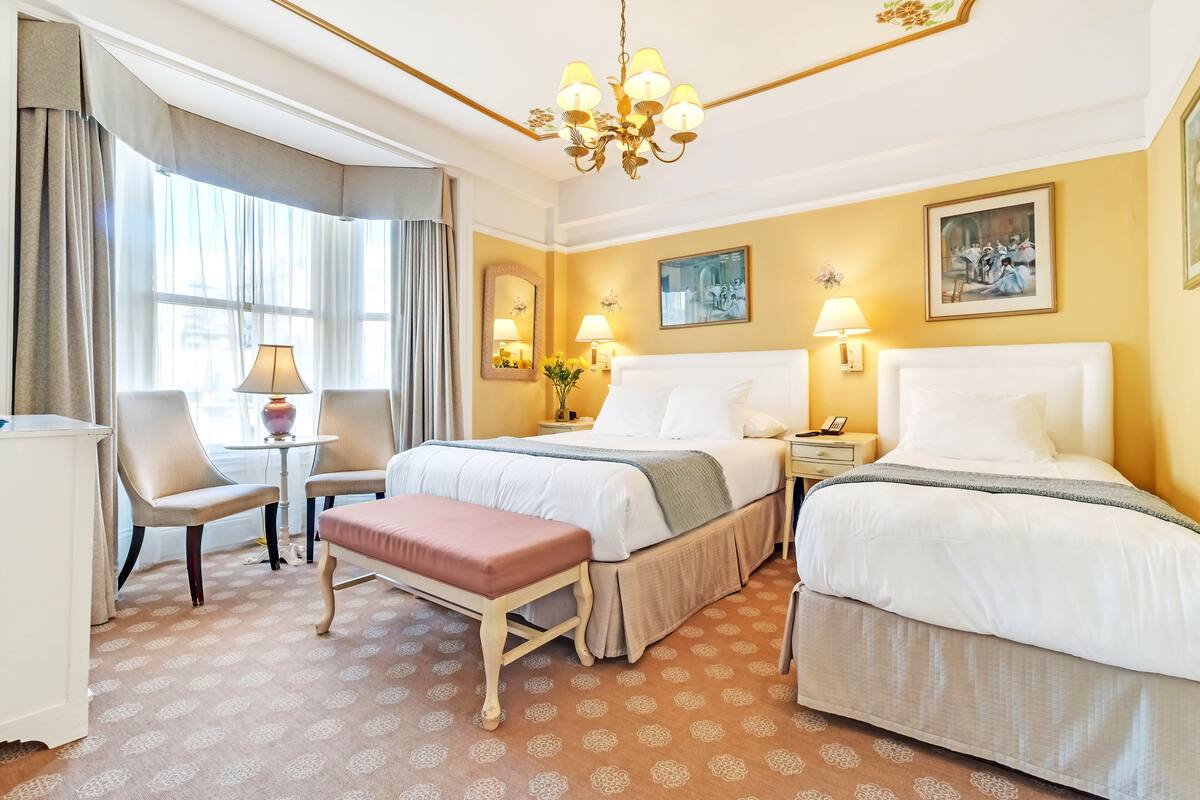 Une chambre d’hôtel avec deux lits, un bureau, une chaise, un banc et un lustre.