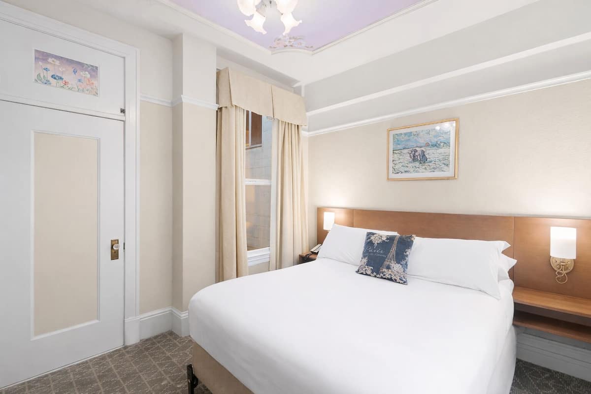 Une chambre d’hôtel avec un grand lit, une table de chevet, une lampe fixée au mur et un tableau.