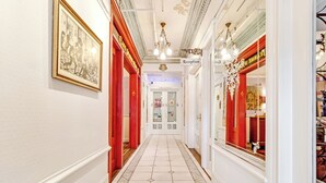 A hallway with a reception area, red doors, and a chandelier. - Cornell Hotel (San Francisco)
