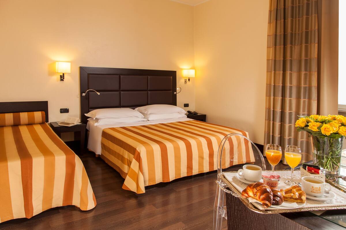 A hotel room with two beds, a breakfast tray with croissants, coffee, and juice, and a vase of yellow flowers.