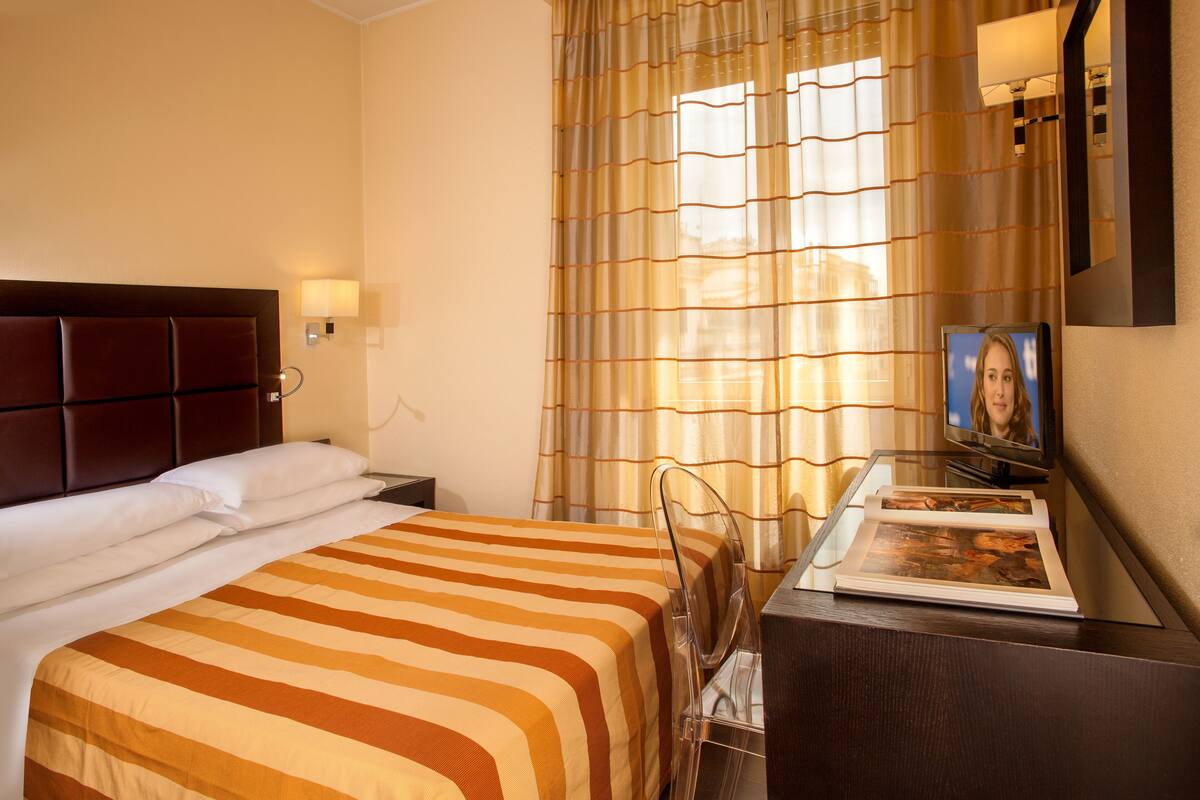 A hotel room with a large bed, a desk with a chair, a television, and a window with curtains.