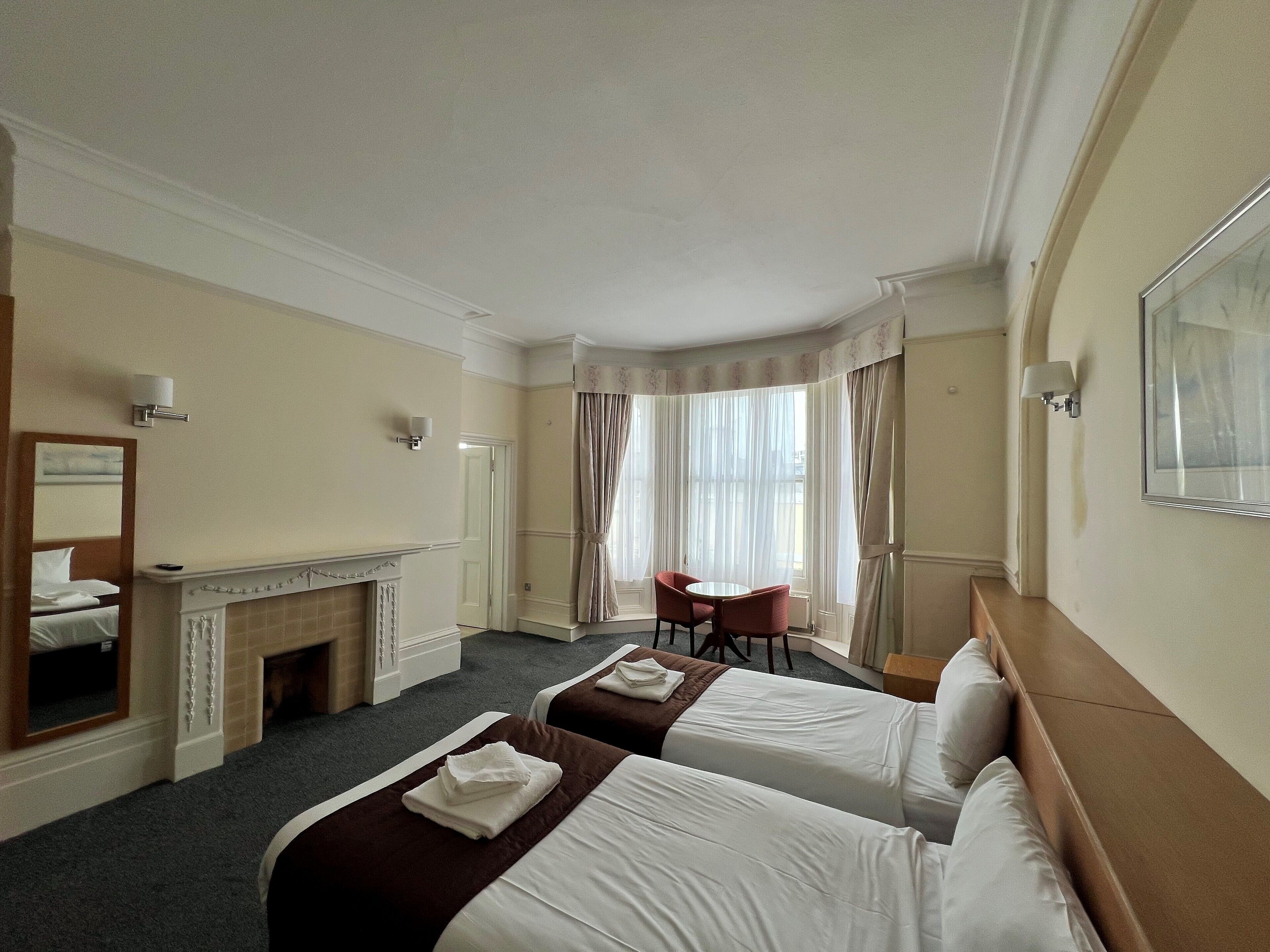 A hotel room with two beds, a fireplace, a desk, and a chair.