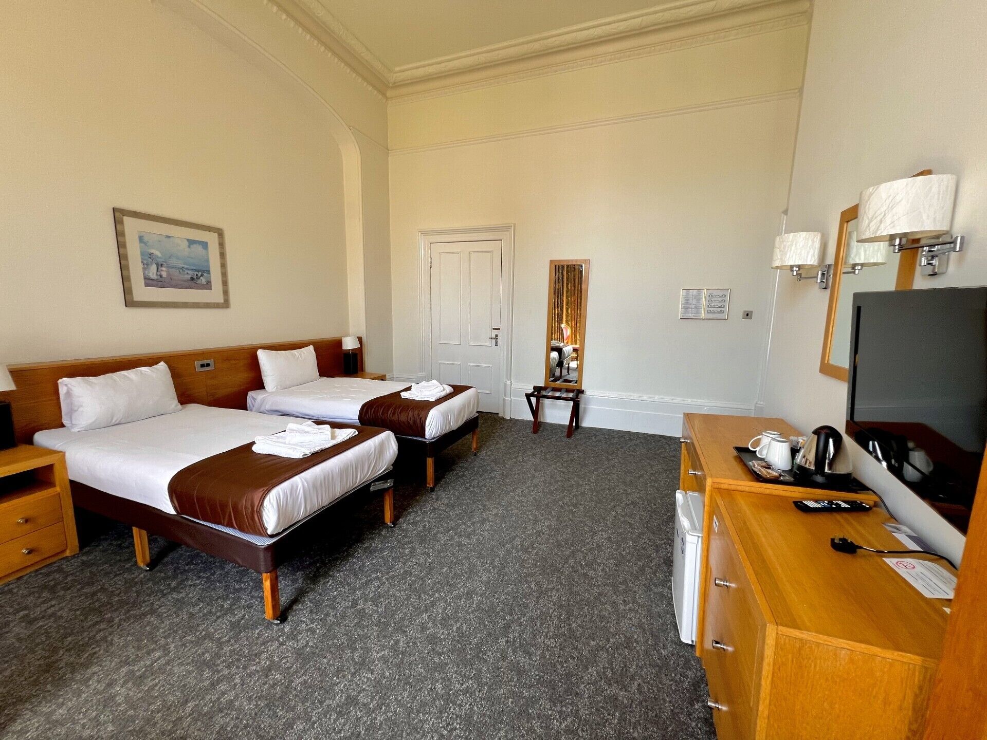 A hotel room with two beds, a desk with a TV, and a mirror.