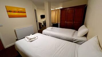 Une chambre d’hôtel avec deux lits simples, un radiateur, un tableau représentant un coucher de soleil, une armoire et un téléviseur.