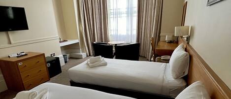A hotel room with two beds, a desk with a computer, a TV, and a window with curtains.