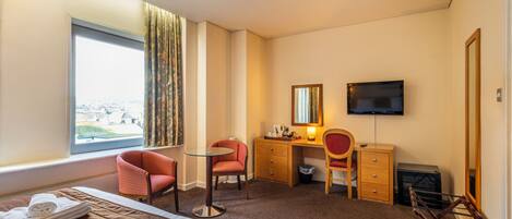 A hotel room with a bed, two chairs, a desk, a television, and a window with curtains.